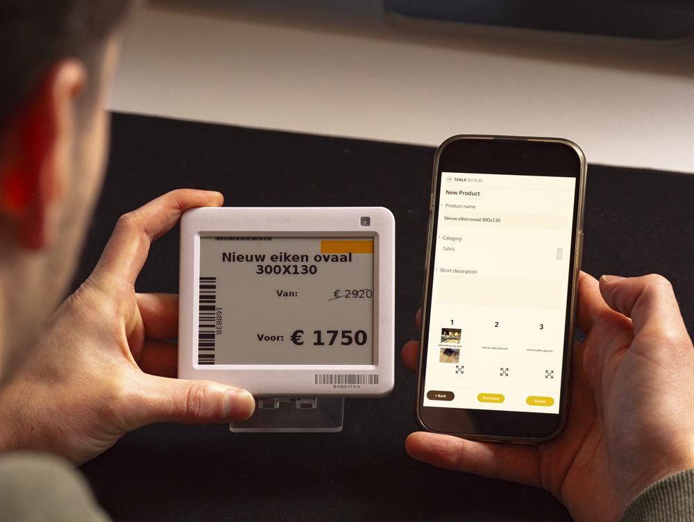Een e-paper prijskaartje toont de nieuwe prijs van 1750 euro naast de doorgestreepte 2920, terwijl dezelfde productgegevens in de app op de telefoon staan.